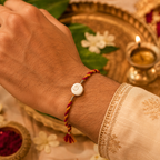Gomti Chakra rakhi with red and yellow braided thread tied on a wrist, styled with a traditional pooja thali, diya, kumkum, and festive decor.