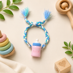 Baby milk bottle rakhi with blue and white braided thread displayed on a soft cream background with wooden baby toys and green leaves.