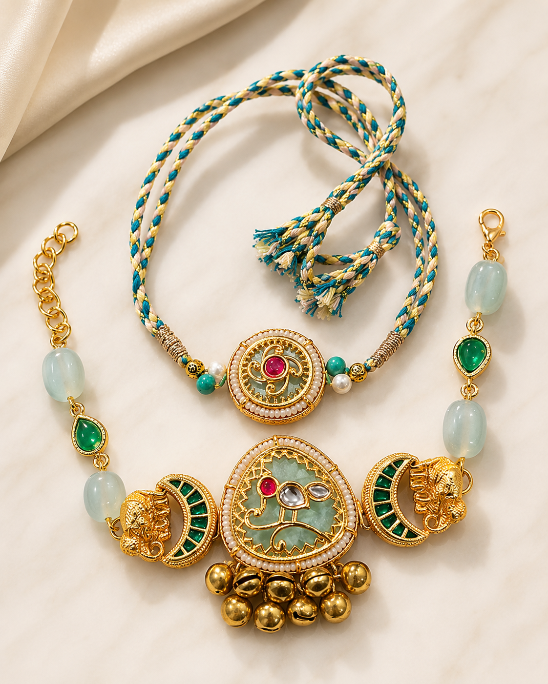 Gold and green bhaiya bhabhi rakhi set with elephant charms, kundan stones, pearl details, gold bells, and braided rakhi thread on white marble.