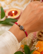 Om rudraksha rakhi with red thread tied on a wrist, styled with festive diya, flowers, and traditional Raksha Bandhan decor.