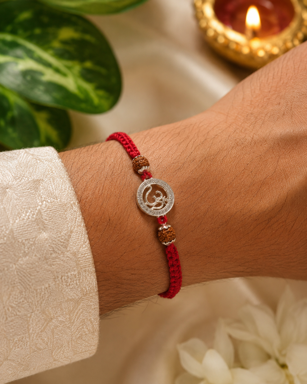 Silver Om rudraksha rakhi with red braided thread tied on a male wrist in a premium Raksha Bandhan setting.
