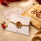 Red Jadau Kudan rakhi displayed on a House of RangReethi card with gold potli, roli chawal bottles, and Raksha Bandhan greeting cards.