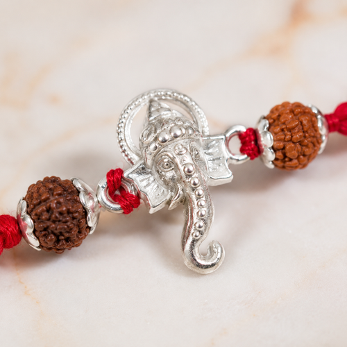 Close-up of silver Ganesh rakhi with rudraksha beads, red thread, and detailed  design.