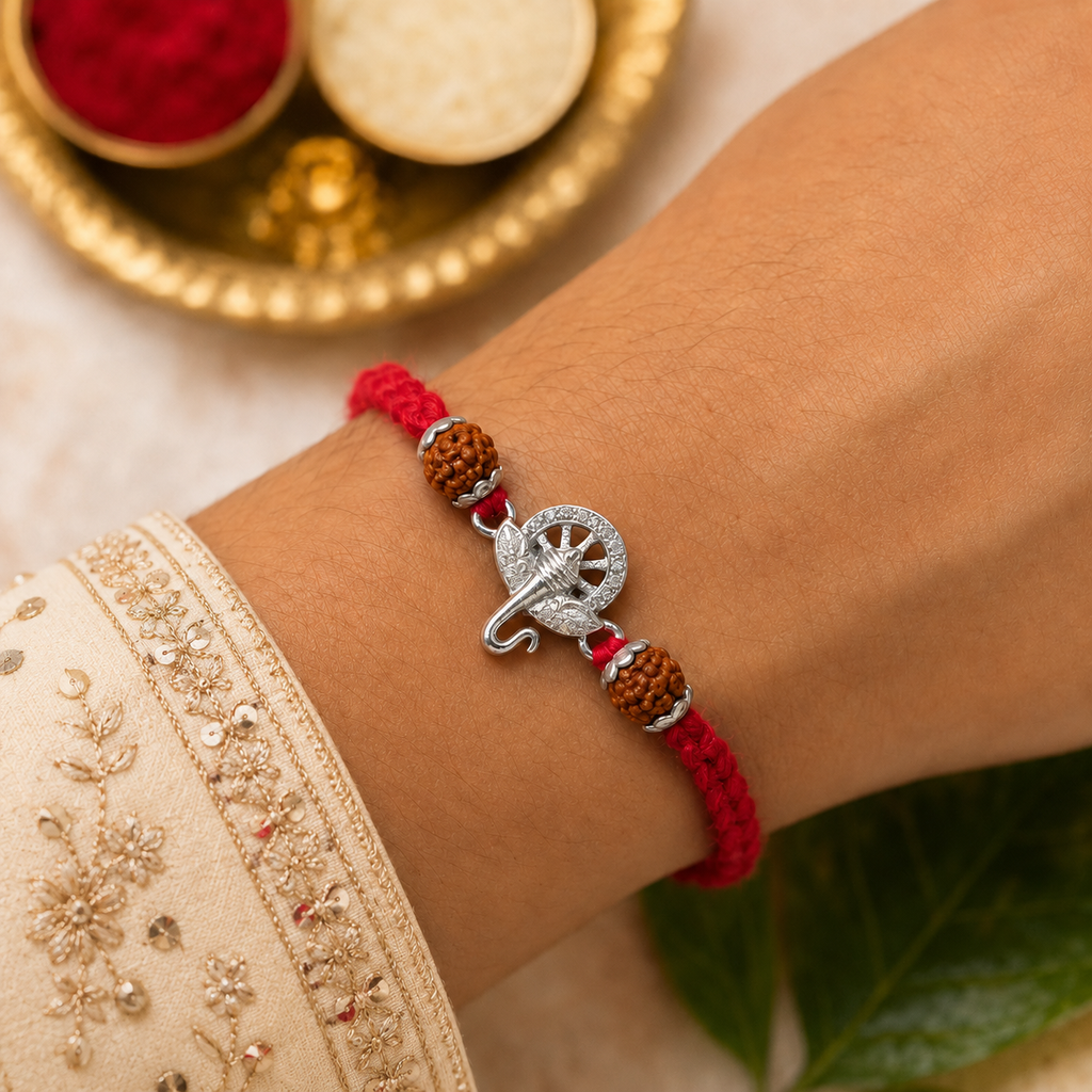 Silver Ganesh rudraksha rakhi with red thread tied on a wrist, styled with a traditional pooja thali, kumkum, rice, and festive deco