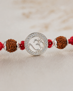 Close-up of silver Om rakhi pendant with diamond-style border, rudraksha beads, silver spacers, and red braided thread.