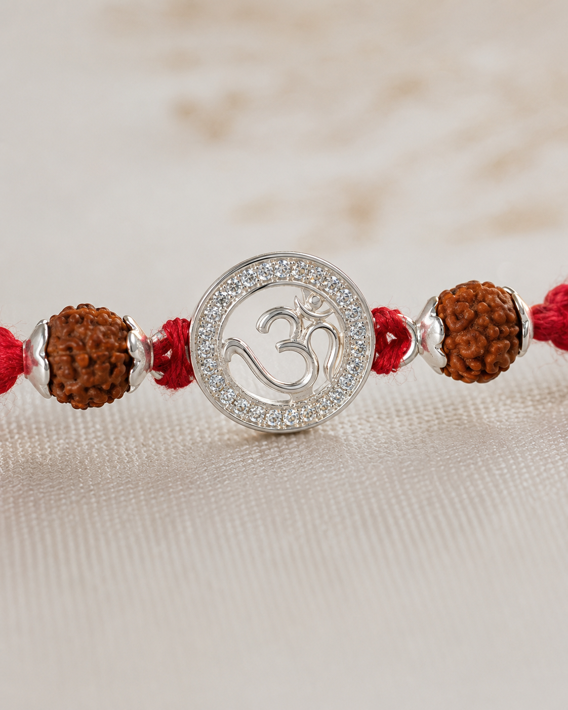 Close-up of silver Om rakhi pendant with diamond-style border, rudraksha beads, silver spacers, and red braided thread.