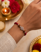 Silver Swastik rudraksha rakhi with red thread tied on a wrist, styled with a traditional pooja thali, diya, rice, and festive flowers.