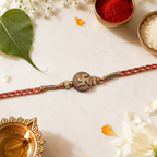 Swastik wooden rakhi with red braided thread, gold beads, roli, chawal, diya, and festive leaf on a premium cream background.